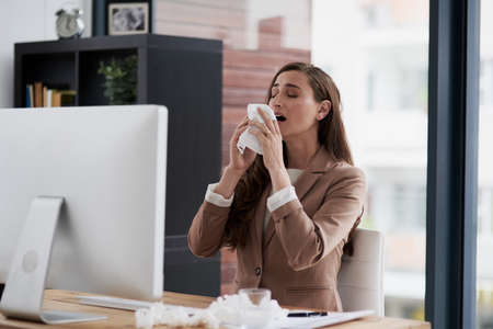Too many sneezes are interrupting her way towards success. Shot of a young businesswoman suffering with allergies at work.の写真素材