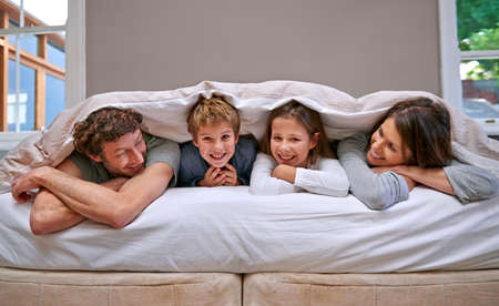 Family time. Shot of a happy family of four in the bedroom.の写真素材