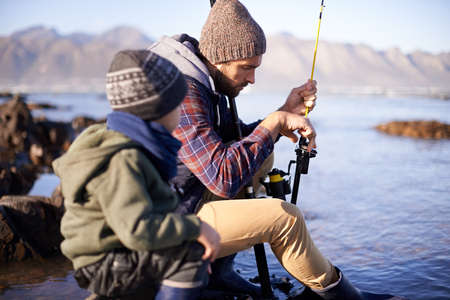 And then you turn this around here. Shot of a cute little boy fishing with his father by the sea.の写真素材