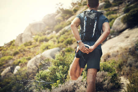 Warming up while taking in the view. Rearview shot of an unrecognizable young man stretching before heading off on his hike in the mountains.の写真素材
