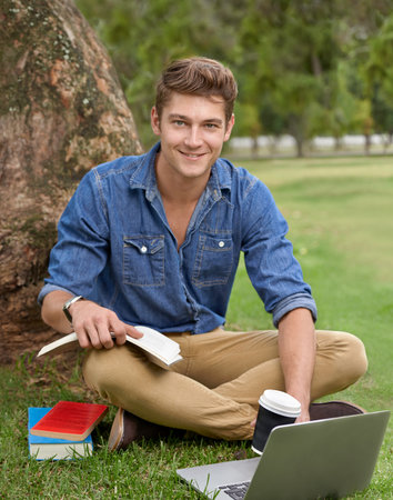 This is better than the library. Portrait of a handsome young man studying in the park with a laptop.の写真素材