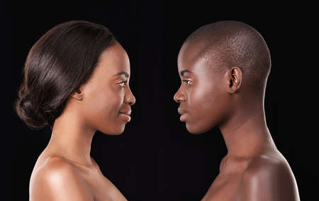 Perfect profiles. Two beautiful african women standing face to face against a black background.の写真素材