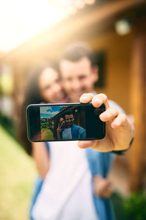 Capturing their love. Cropped shot of an affectionate young couple taking selfies outside with their house in the background.の写真素材