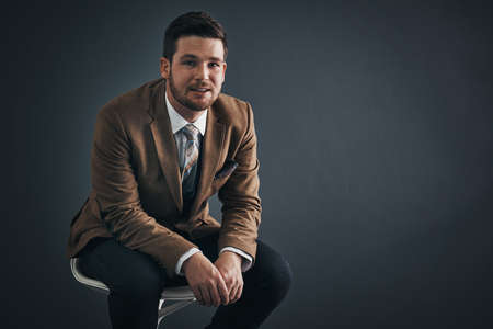 Keep confidence in your stride as you proceed. Studio portrait of a handsome young businessman sitting on a chair against a dark background.の写真素材