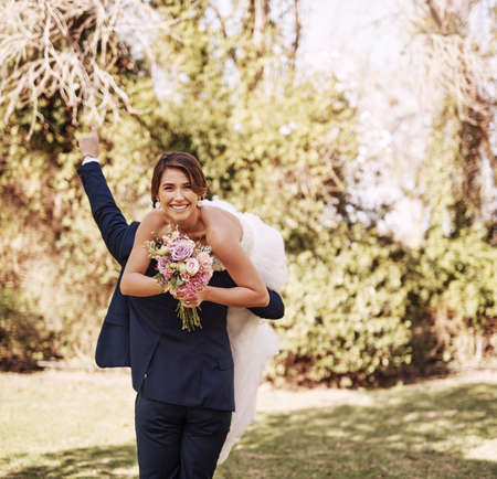 Hes finally taking me home as his wife. Cropped shot of a beautiful young bride smiling while her groom carries her on their wedding day.の写真素材
