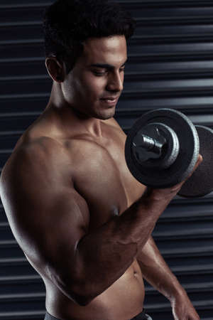 Building big and bulging biceps. Cropped shot of an athletic young man working out with a dumbbell.の写真素材