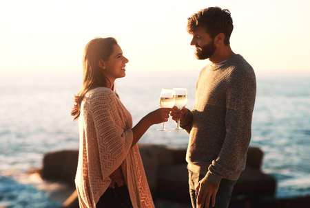 I want to do everything in this life with you. Shot of a happy young couple toasting with wine at the beach.の写真素材
