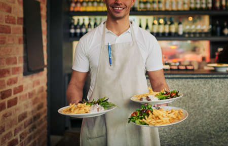I got what you ordered right here sir. Shot of an unrecognizable waiter holding three plates of food that hes going to serve to customers inside of a restaurant during the day.の写真素材