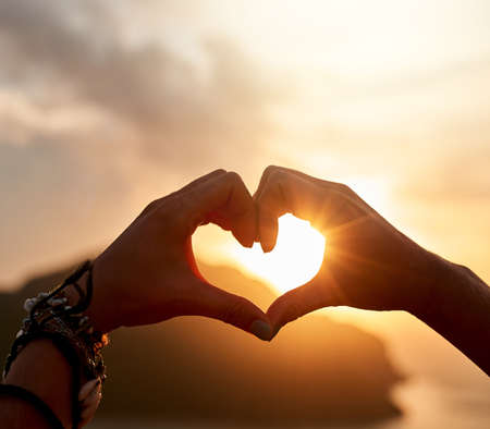 Loving this holiday feeling. Cropped shot of an unidentifiable person making a heart shape with their hands at sunset.の写真素材
