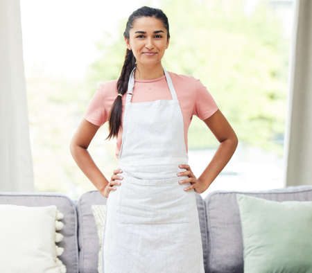 Today is chores day so tomorrow can be chill day. Shot of a young woman wearing an apron while busy cleaning at home.の写真素材