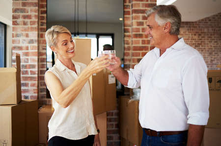 Welcome home honey. Shot of a mature couple toasting with water after a successful day moving house.の写真素材
