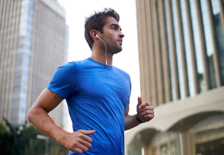 Running along his favorite city route. Shot of a young man jogging through the city.の写真素材