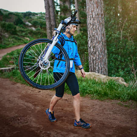 No weekend is complete without a bike ride. Shot of a male cyclist walking along a trail carrying his mountain bike.の写真素材