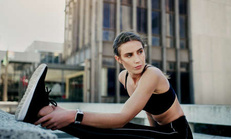 Working on herself with every workout. Shot of a young woman stretching during her workout in the city.の写真素材