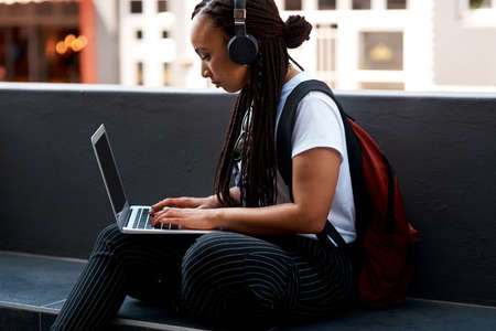 Get connected, get busy. Shot of an attractive young woman listening to music and using her laptop...