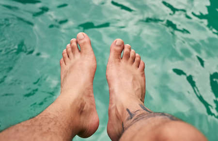 Getting a feel for the water. High angle shot of a mans feet above the water.の写真素材