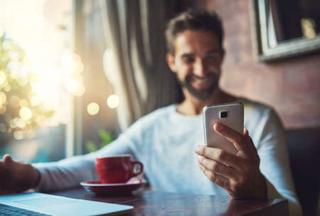 Smiling at an SMS. Cropped shot of a young man using his cellphone in a coffee shop.