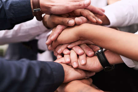 We work better when we get together as one. Closeup shot of an unrecognizable group of businesspeople joining their hands in a huddle.の写真素材