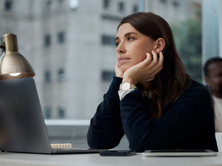 Dreaming about sunny skies. Shot of a young businesswoman looking bored at work.の写真素材