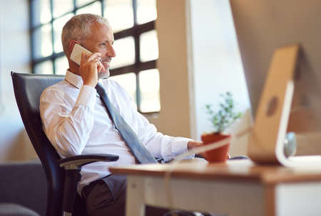 Hes the man everybody wants to talk to. Shot of a mature businessman using his phone in the office.