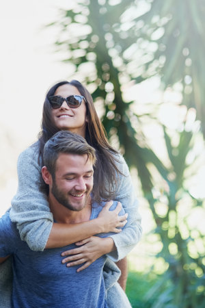Fun and in love. Shot of a young man giving his girlfriend a piggyback while enjoying a day together outside.の写真素材