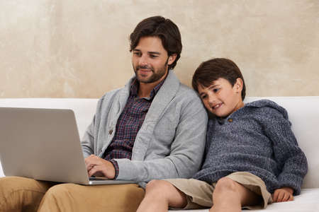 Browsing the web together. A young boy and his father using a laptop.