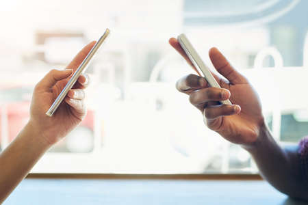 Ill give you mine if you give me yours. Shot of two unidentifiable friends using their smartphones together.の写真素材