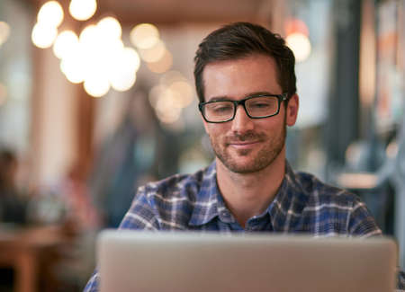 The free wifi here makes it a no brainer. Shot of a young man using his laptop while sitting in a coffee shop.の写真素材