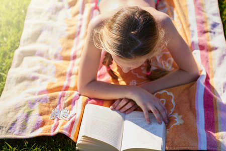 Get lost in a good piece of literature. Shot of a teenage girl lying on a towel while reading a...