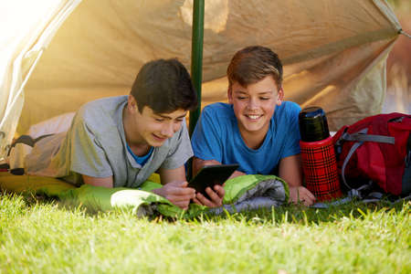 They brought some entertainment along. A young boy showing his friend something on a digital tablet while theyre camping.