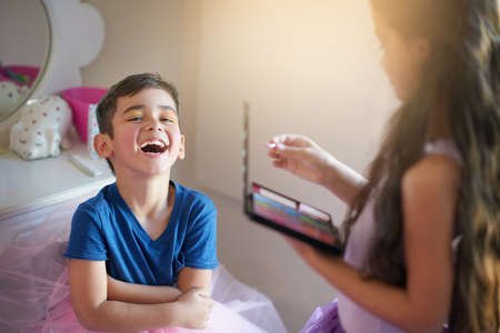 Im just getting in touch with my feminine side. Shot of a cute little girl playing makeover with her brother at home.の写真素材