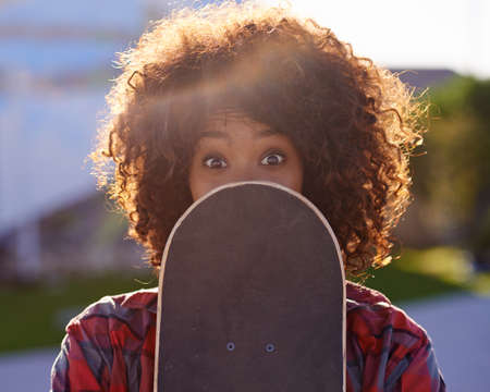 A little fun in the skate park. A young woman with a quirky expression holding her skateboard.の写真素材