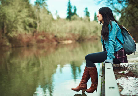 The water looks amazing. Shot of a young woman sitting by a lake outdoors.の写真素材