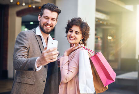 Why not spoil your selfie. Shot of a young couple taking a selfie while out shopping.の写真素材
