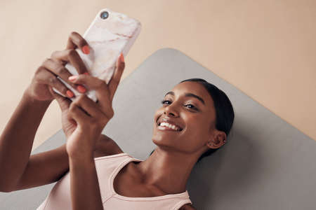 Post-gym selfie. Shot of an attractive young woman lying down on a yoga mat and using her cellphone...