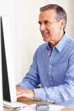 Smiling mature man calculating expenses using computer. Portrait of a smiling mature man calculating...