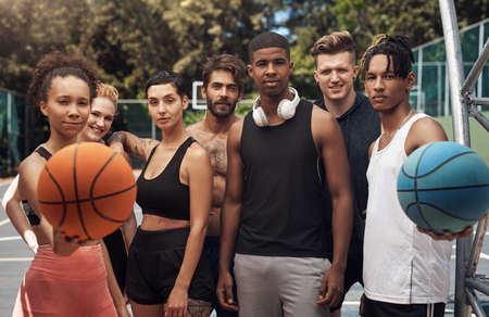 Becoming part of a team and a larger community. Portrait of a group of sporty young people standing together on a sports court.の写真素材