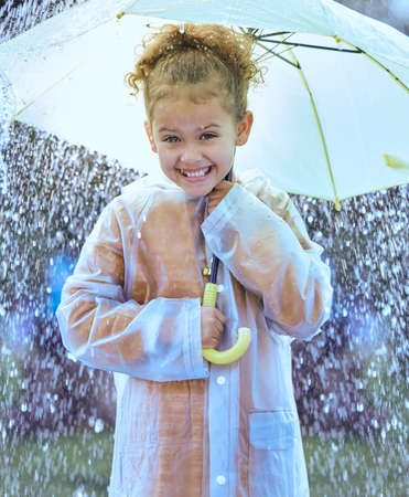 This is so exciting. Shot of a little girl playfully standing in the rain holding her umbrella.