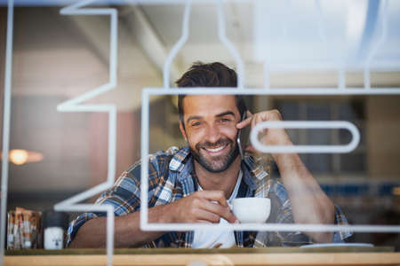 Staying connected during his coffee break. Portrait of a happy young man answering his cellphone...