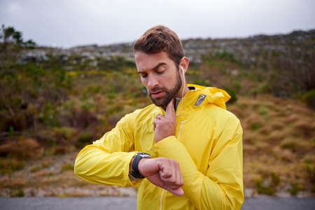 Focus on cardio. Shot of a handsome young man checking his heart rate while running in rainy...
