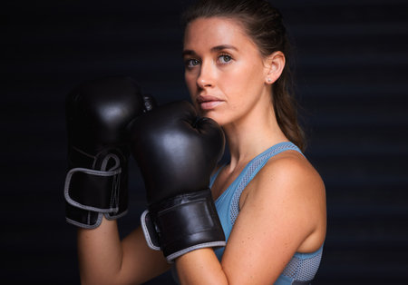 Unbreakable and undefeated. Portrait of a young woman wearing boxing gloves against a black background.の写真素材