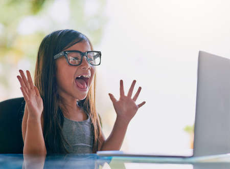 Technology excites her. Cropped shot of a little girl looking excited while using a laptop.の写真素材