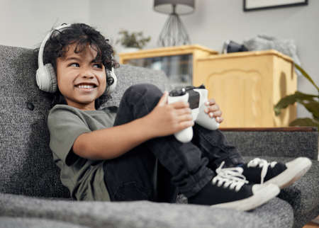 My homework is done and now its time for some fun. Shot of an adorable little boy wearing headphones while playing video games at home.の写真素材