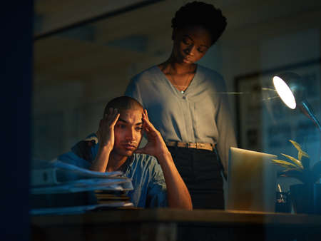I never seem to see the end of my deadlines. Cropped shot of a young businessman looking stressed out while a colleague tries to console him.の写真素材