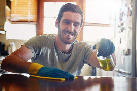 Keeping his home completely spotless. Cropped shot of a young man cleaning a kitchen surface at home.の写真素材