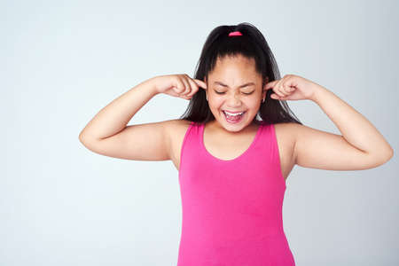 No...no...NOOO. Studio shot of a cute young girl with her fingers in her ears against a gray background.の写真素材