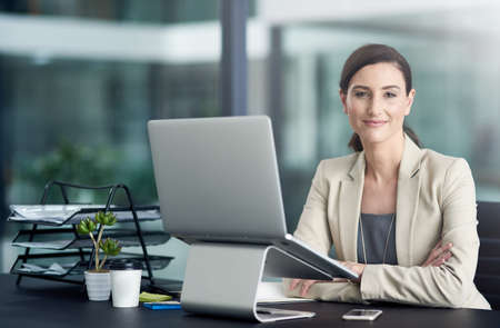 Job satisfaction pays off. Portrait of a professional businesswoman using a laptop at her office desk.の写真素材