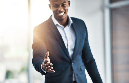 Its a pleasure to meet you. Cropped portrait of a handsome young businessman offering his hand while standing in his modern office.の写真素材
