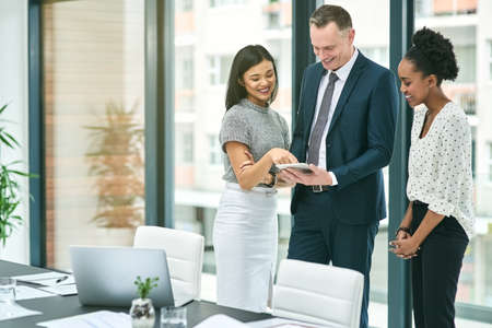 I think this works really well. Cropped shot of three businesspeople looking over a tablet in the...