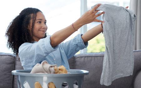 That detergent really did get all the stains out. Shot of a young woman folding away her freshly cleaned laundry at home.の写真素材